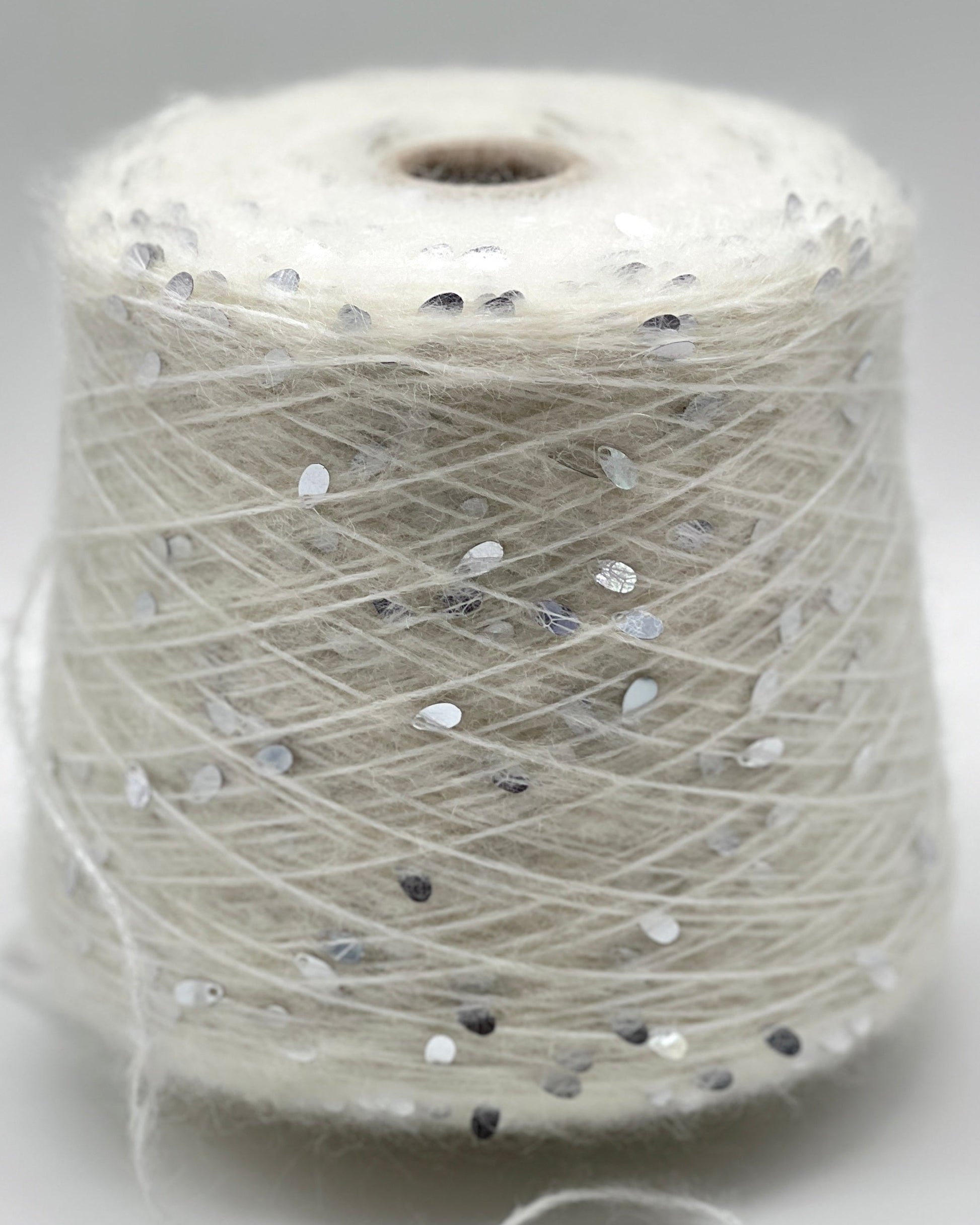 Spool of white thread with small black and gray dots on a light gray background