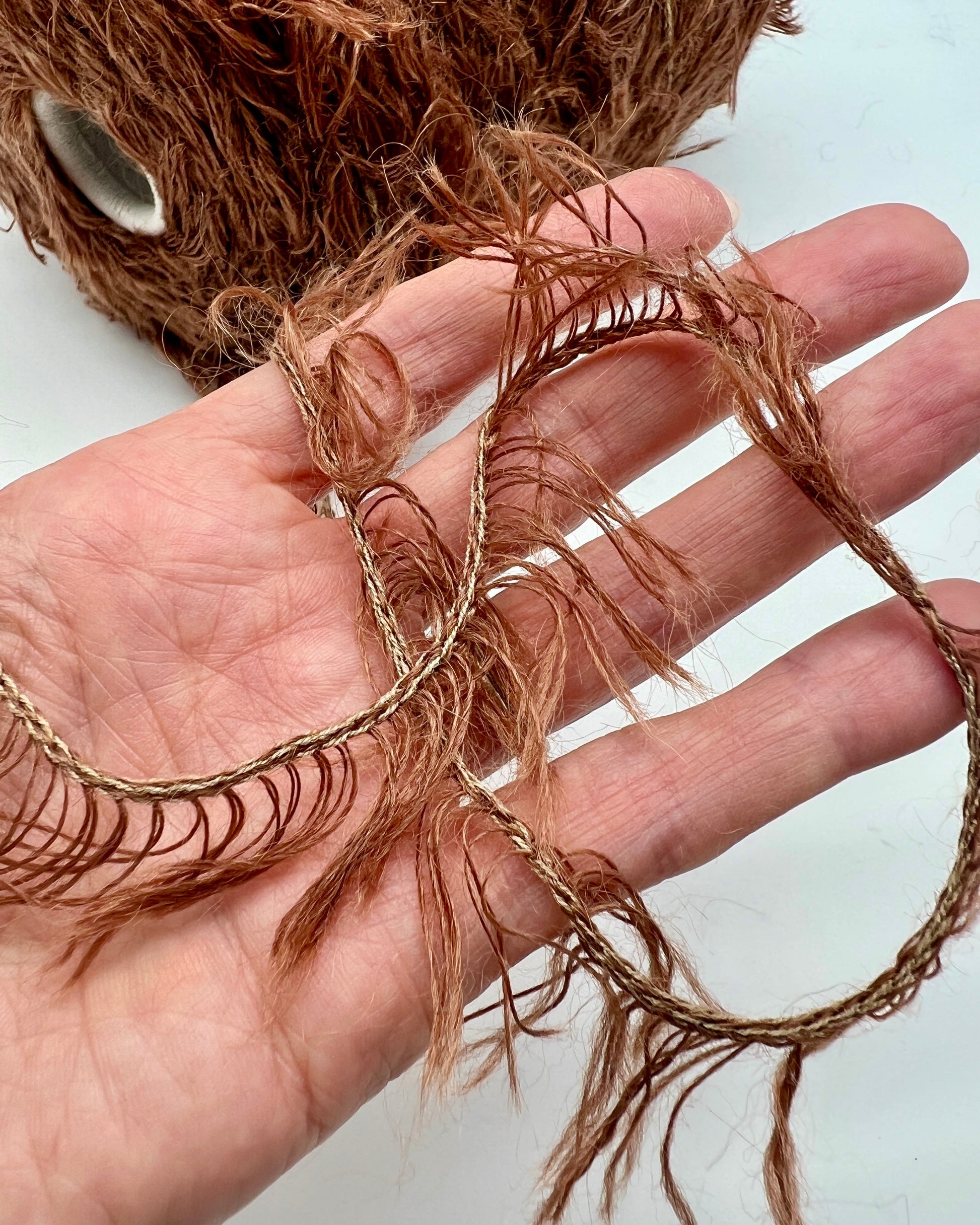 Hand holding a piece of brown hair extensions with a blurred background
