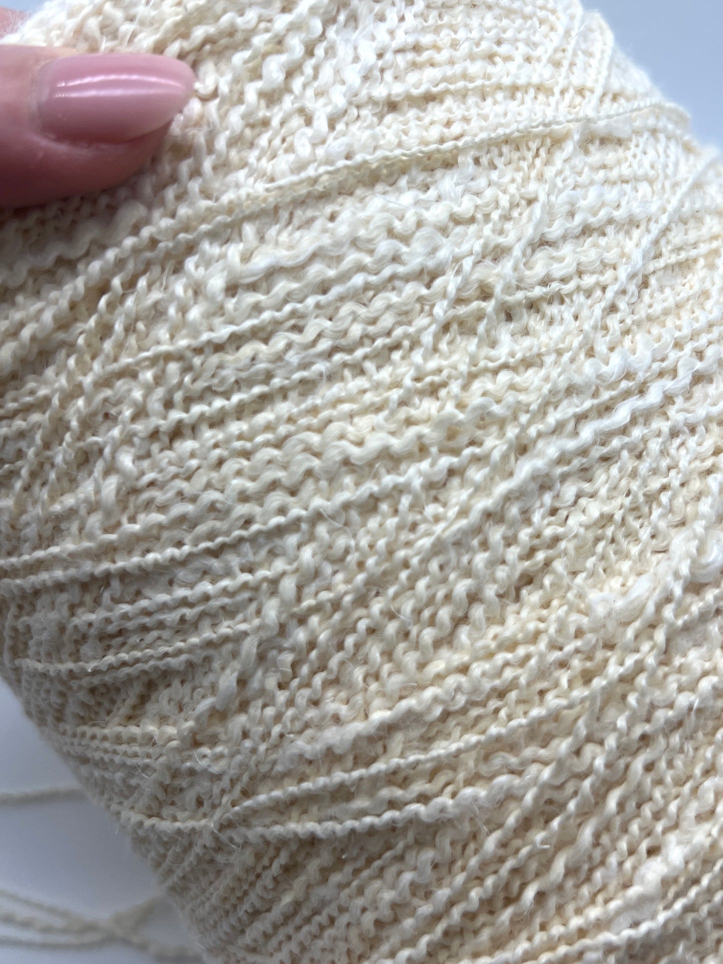 Close-up of a ball of cream-colored yarn with a hand holding it.
