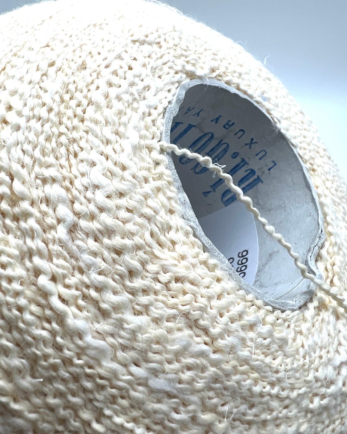 Close-up of a white textured yarn ball with a brand label.