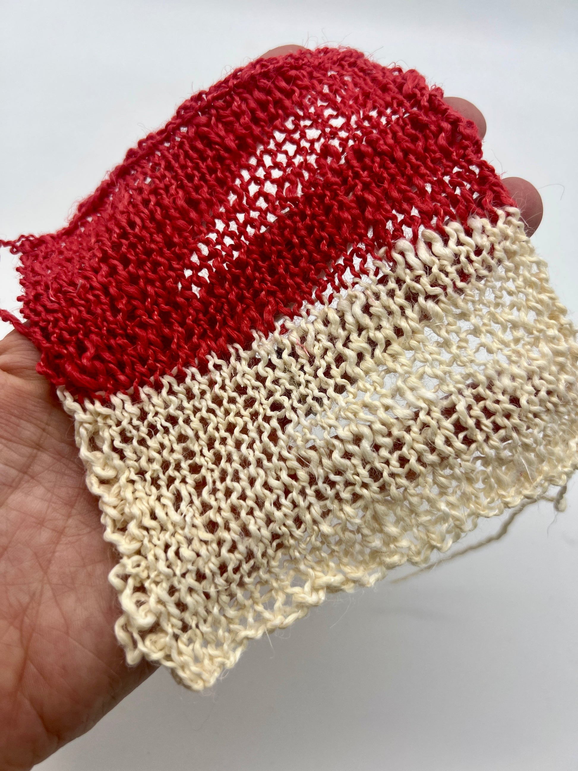 Red and beige knitted fabric held by a hand on a white background