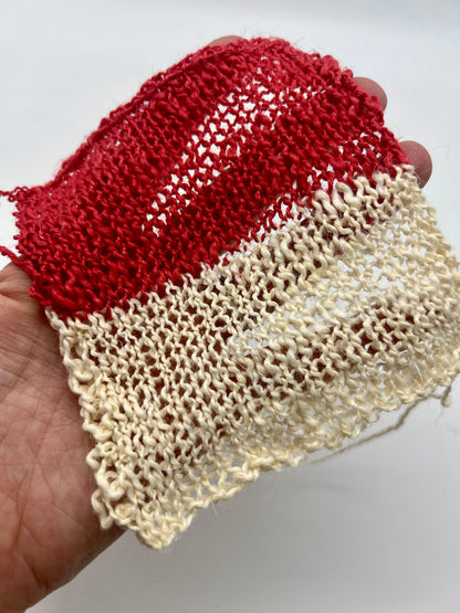Red and beige knitted fabric held by a hand on a white background
