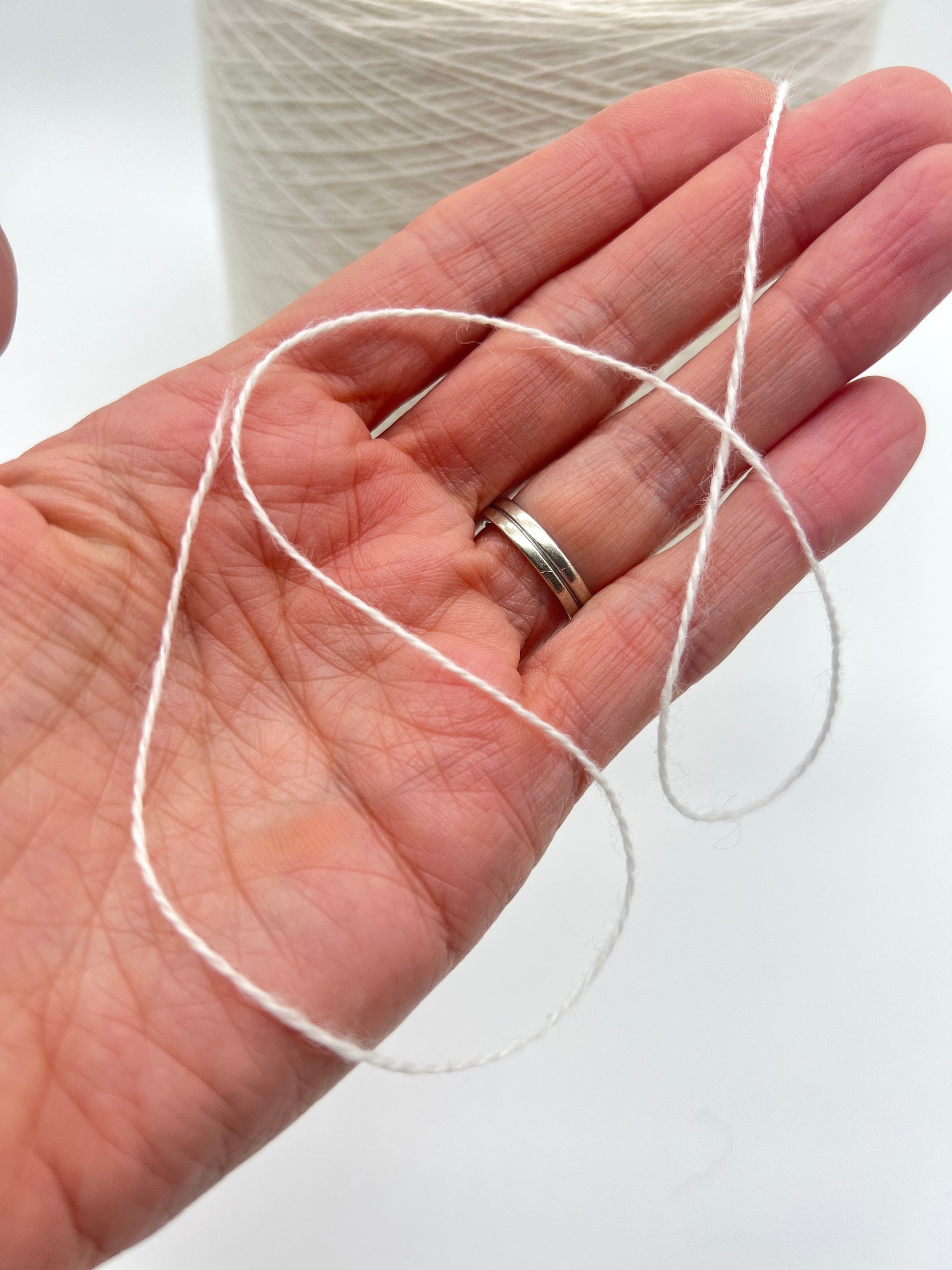 Hand holding a small length of white thread with a spool in the background