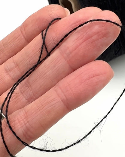 Close-up of a hand holding a black thread against a white background