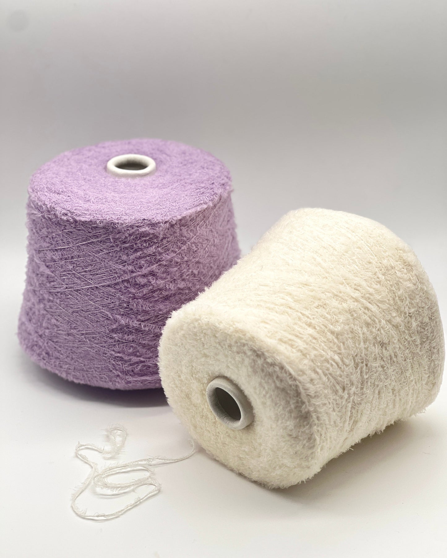 Two spools of yarn, one purple and one white, on a light gray background.