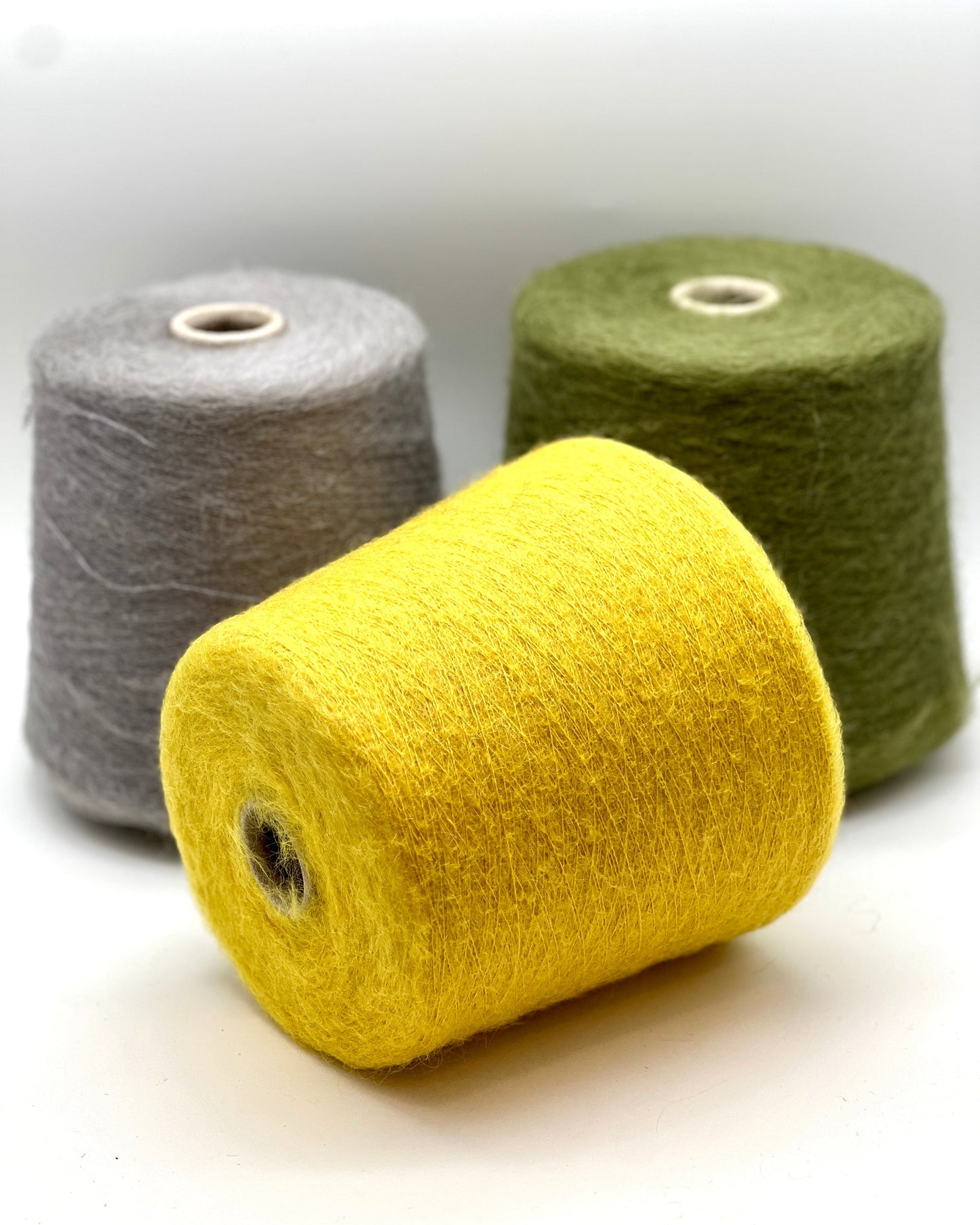 Three spools of yarn in gray, yellow, and green on a white background