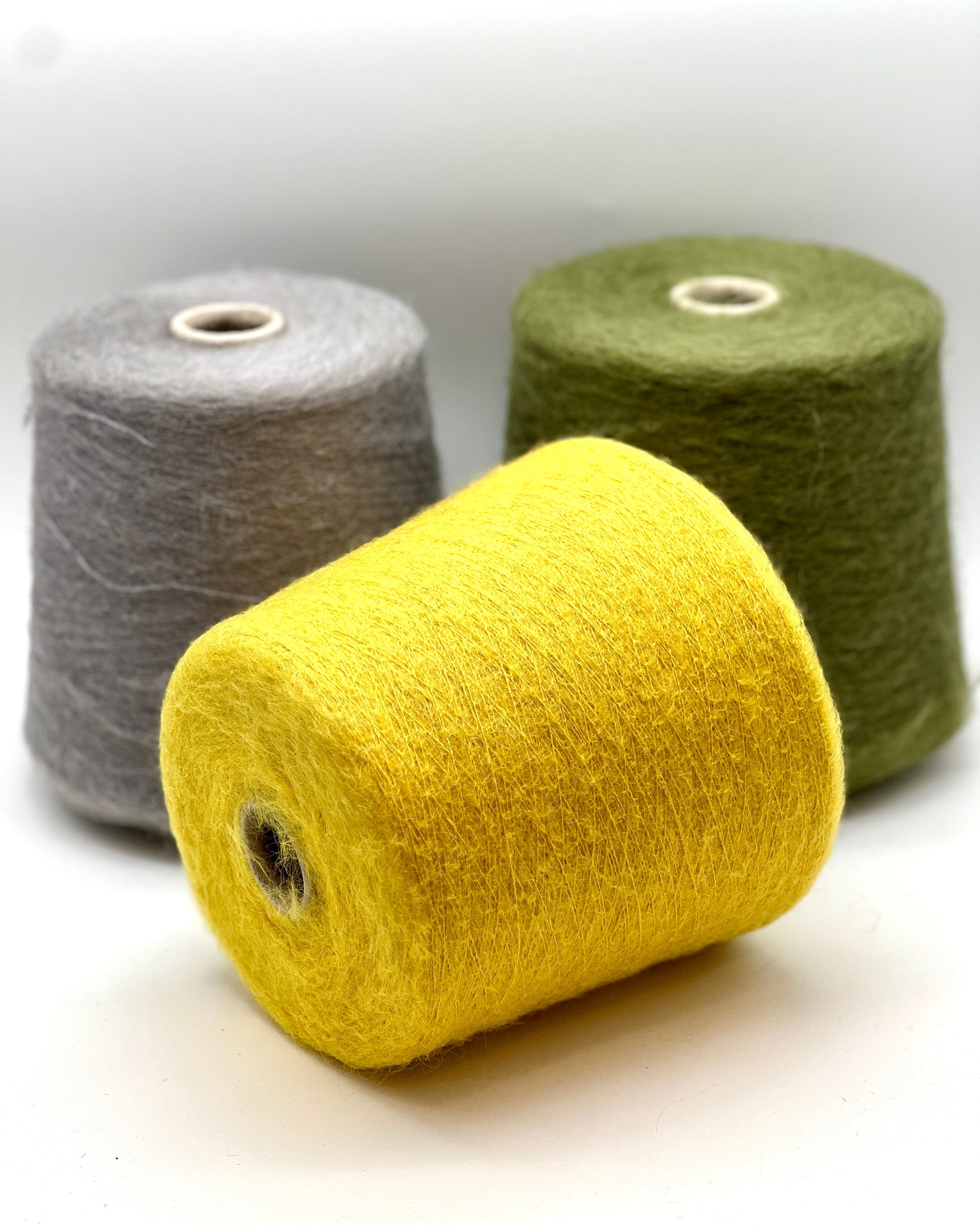 Three spools of yarn in gray, yellow, and green on a white background
