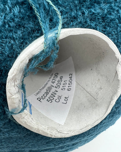 Close-up of a spool of blue yarn with a label on a textured blue background