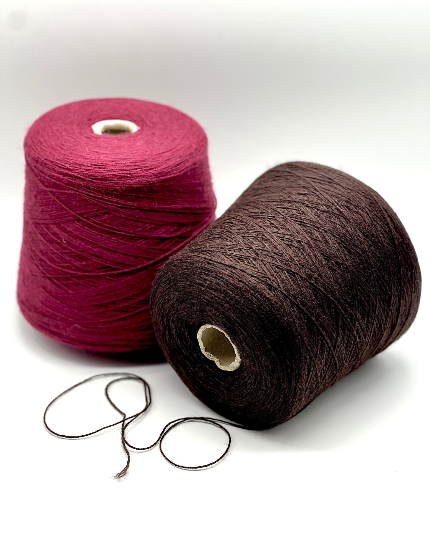 Two spools of yarn, one pink and one brown, on a white background.