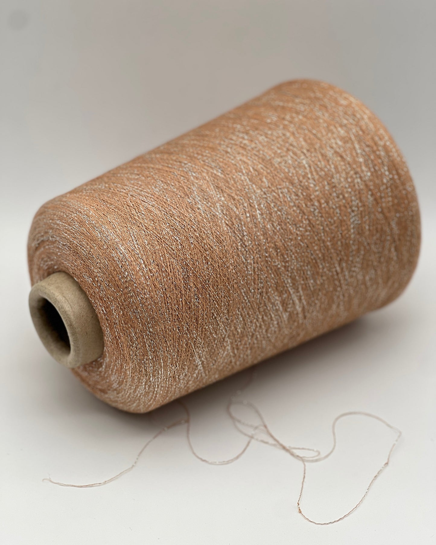 A luxurious cone of Pecci Filati SHIMMER yarn, a modern 50% Cotton, 25% Linen, 14% Polyester, and 12% Polyamide (Lurex) blend. The image showcases the refined metallic glow and delicate texture of this 3400m/100g Italian extrafine yarn, ideal for high-end blending. Authentic luxury fiber available at iDOKNiT.com.