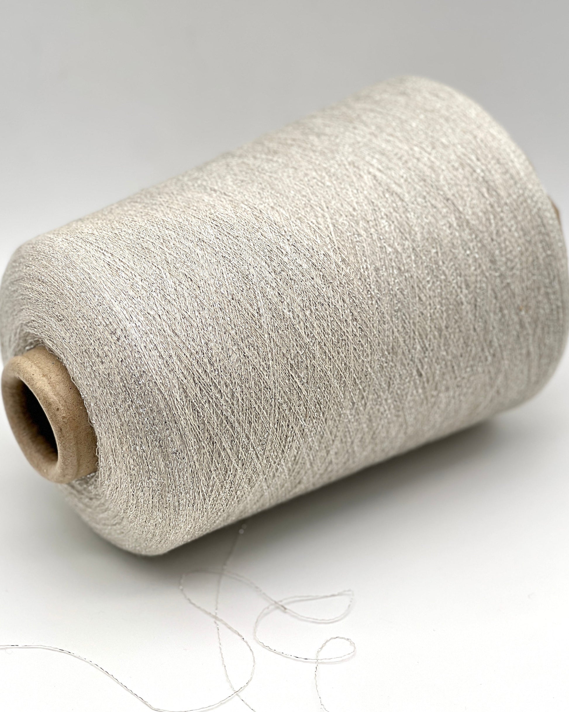 A luxurious cone of Pecci Filati SHIMMER yarn, a modern 50% Cotton, 25% Linen, 14% Polyester, and 12% Polyamide (Lurex) blend. The image showcases the refined metallic glow and delicate texture of this 3400m/100g Italian extrafine yarn, ideal for high-end blending. Authentic luxury fiber available at iDOKNiT.com.