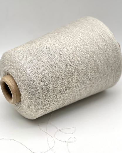 A luxurious cone of Pecci Filati SHIMMER yarn, a modern 50% Cotton, 25% Linen, 14% Polyester, and 12% Polyamide (Lurex) blend. The image showcases the refined metallic glow and delicate texture of this 3400m/100g Italian extrafine yarn, ideal for high-end blending. Authentic luxury fiber available at iDOKNiT.com.