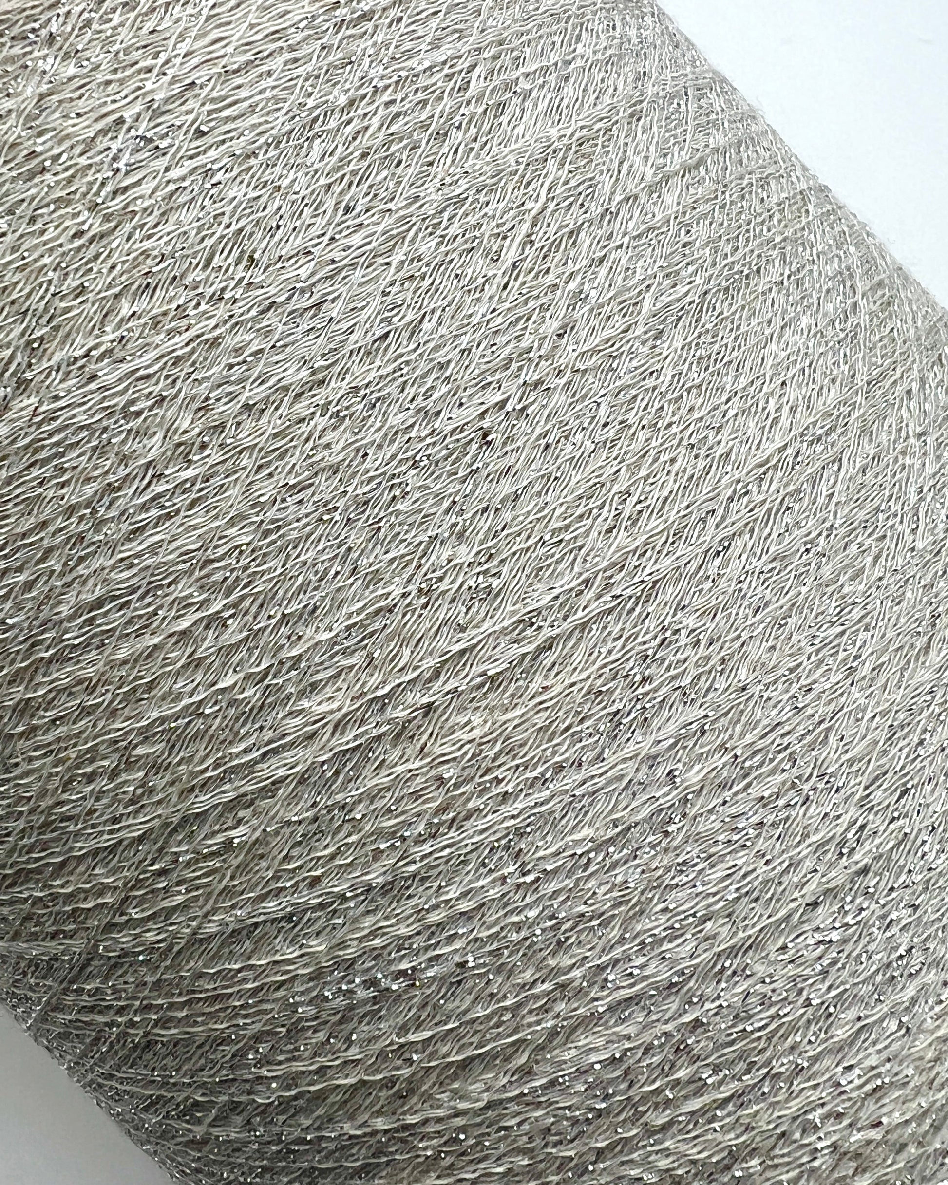 A luxurious cone of Pecci Filati SHIMMER yarn, a modern 50% Cotton, 25% Linen, 14% Polyester, and 12% Polyamide (Lurex) blend. The image showcases the refined metallic glow and delicate texture of this 3400m/100g Italian extrafine yarn, ideal for high-end blending. Authentic luxury fiber available at iDOKNiT.com.
