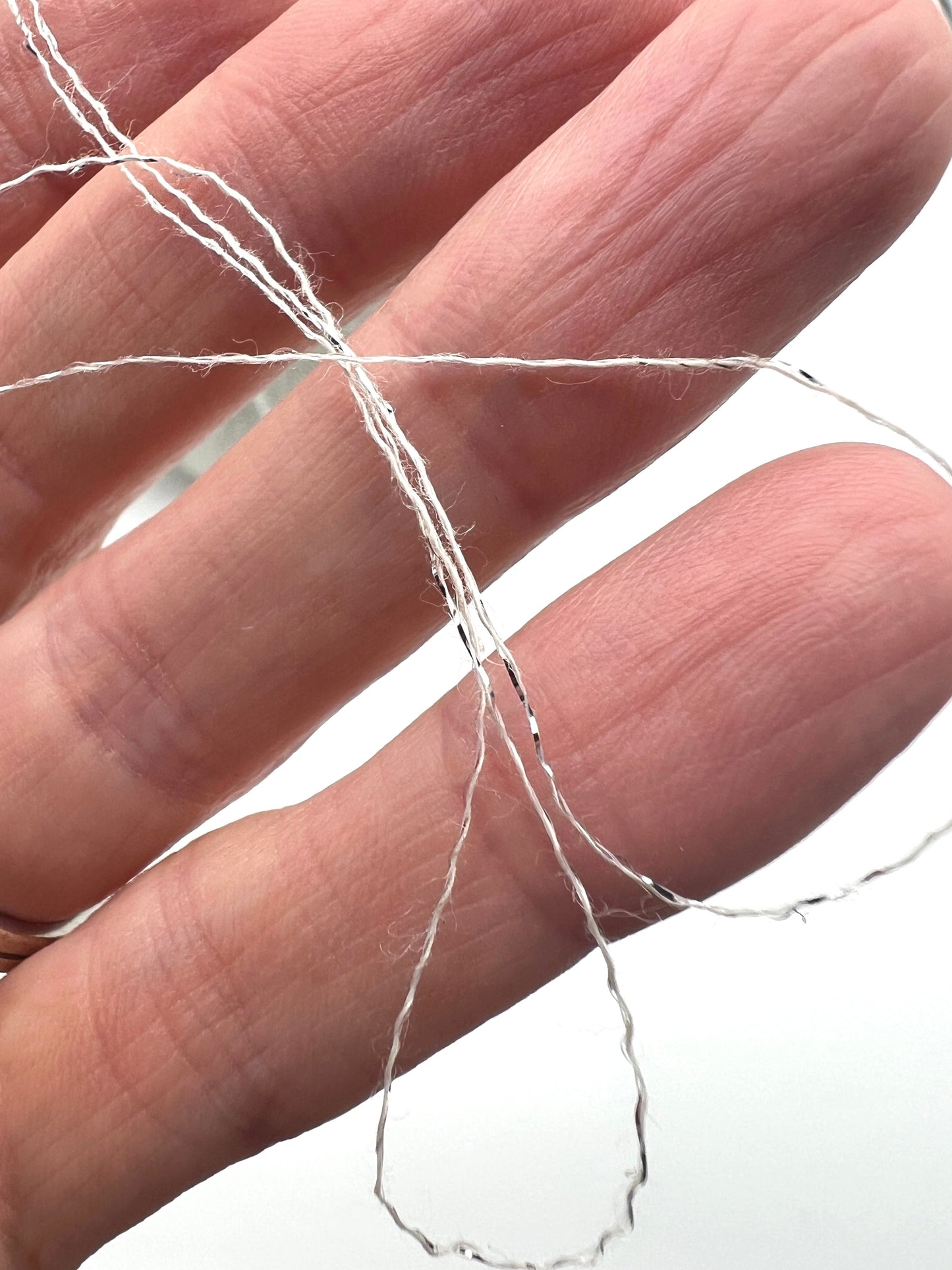 A luxurious cone of Pecci Filati SHIMMER yarn, a modern 50% Cotton, 25% Linen, 14% Polyester, and 12% Polyamide (Lurex) blend. The image showcases the refined metallic glow and delicate texture of this 3400m/100g Italian extrafine yarn, ideal for high-end blending. Authentic luxury fiber available at iDOKNiT.com.