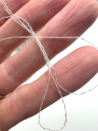 A luxurious cone of Pecci Filati SHIMMER yarn, a modern 50% Cotton, 25% Linen, 14% Polyester, and 12% Polyamide (Lurex) blend. The image showcases the refined metallic glow and delicate texture of this 3400m/100g Italian extrafine yarn, ideal for high-end blending. Authentic luxury fiber available at iDOKNiT.com.