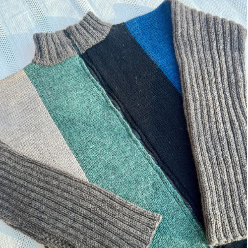 Stack of folded sweaters in various colors on a light background