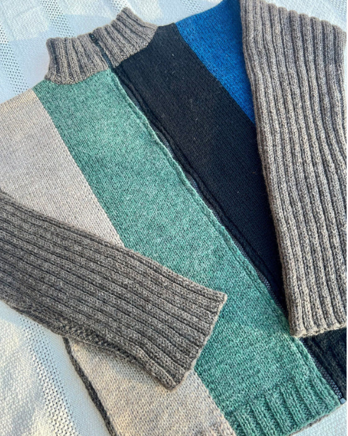 Stack of folded sweaters in various colors on a light background
