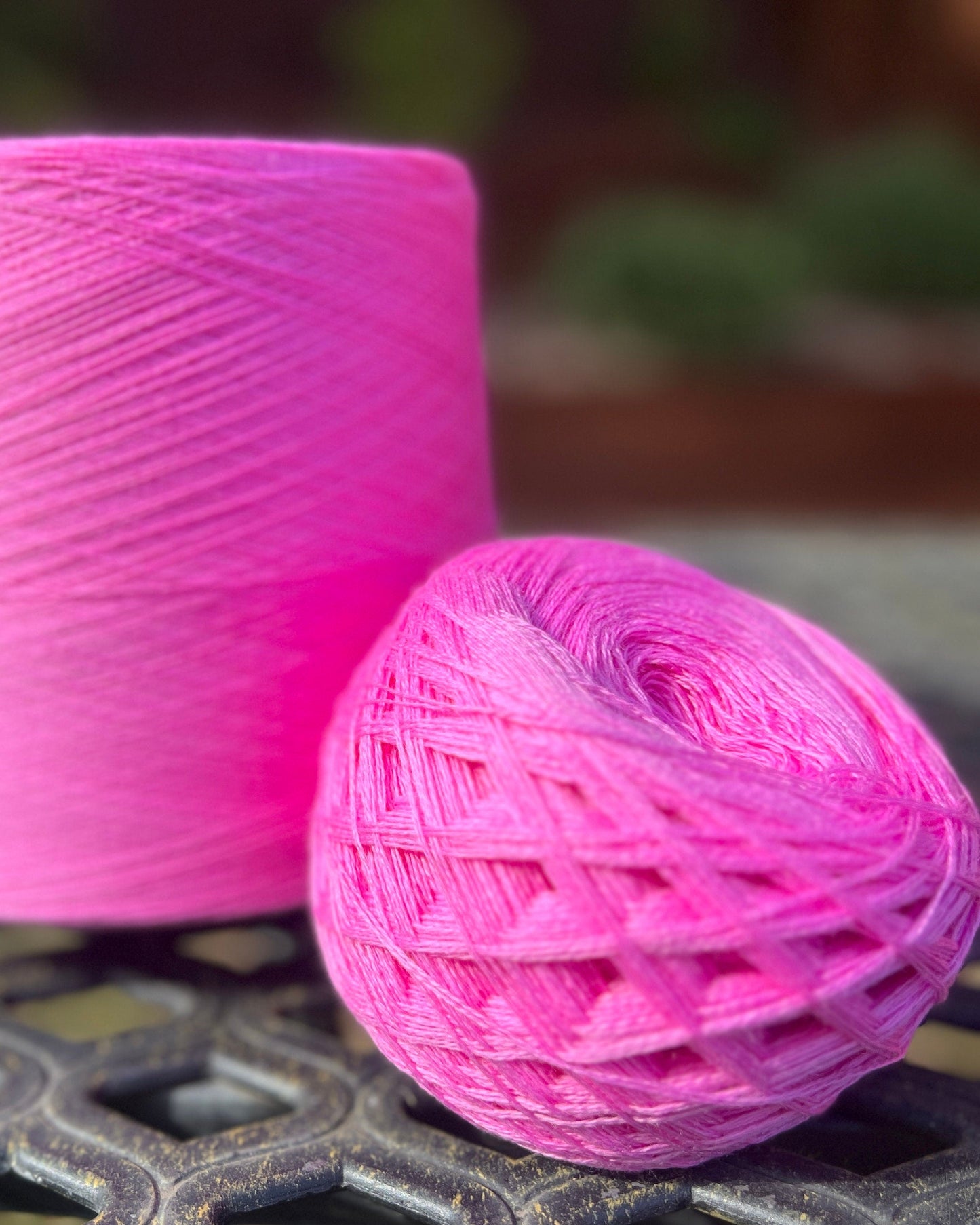 Pink yarn ball and spool on a metal surface with a blurred background