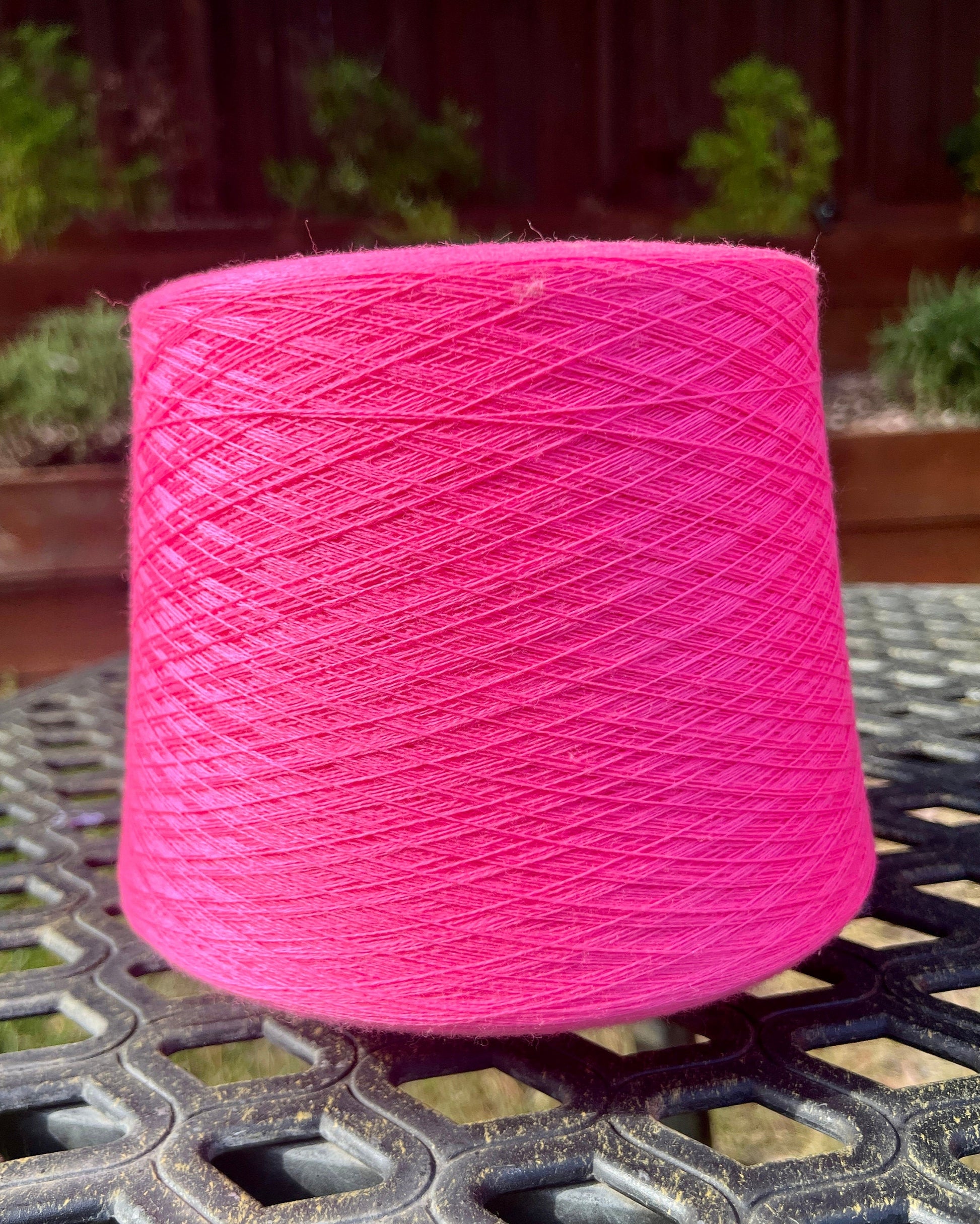 Pink spool of yarn on a metal surface with a blurred outdoor background