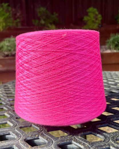 Pink spool of yarn on a metal surface with a blurred outdoor background