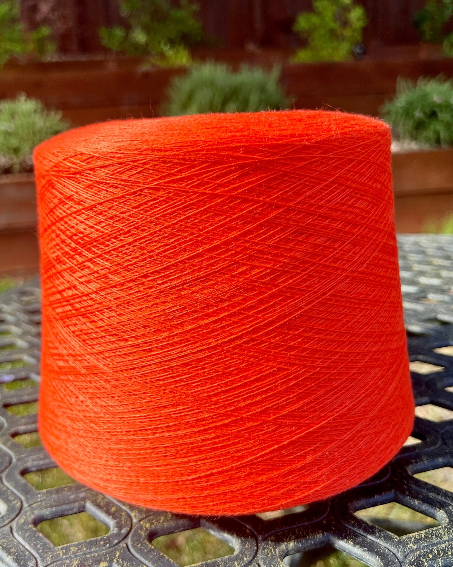 Spool of bright orange yarn on a metal surface with a garden background