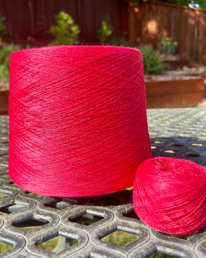 Large spool and smaller ball of red yarn on a metal surface with a garden background