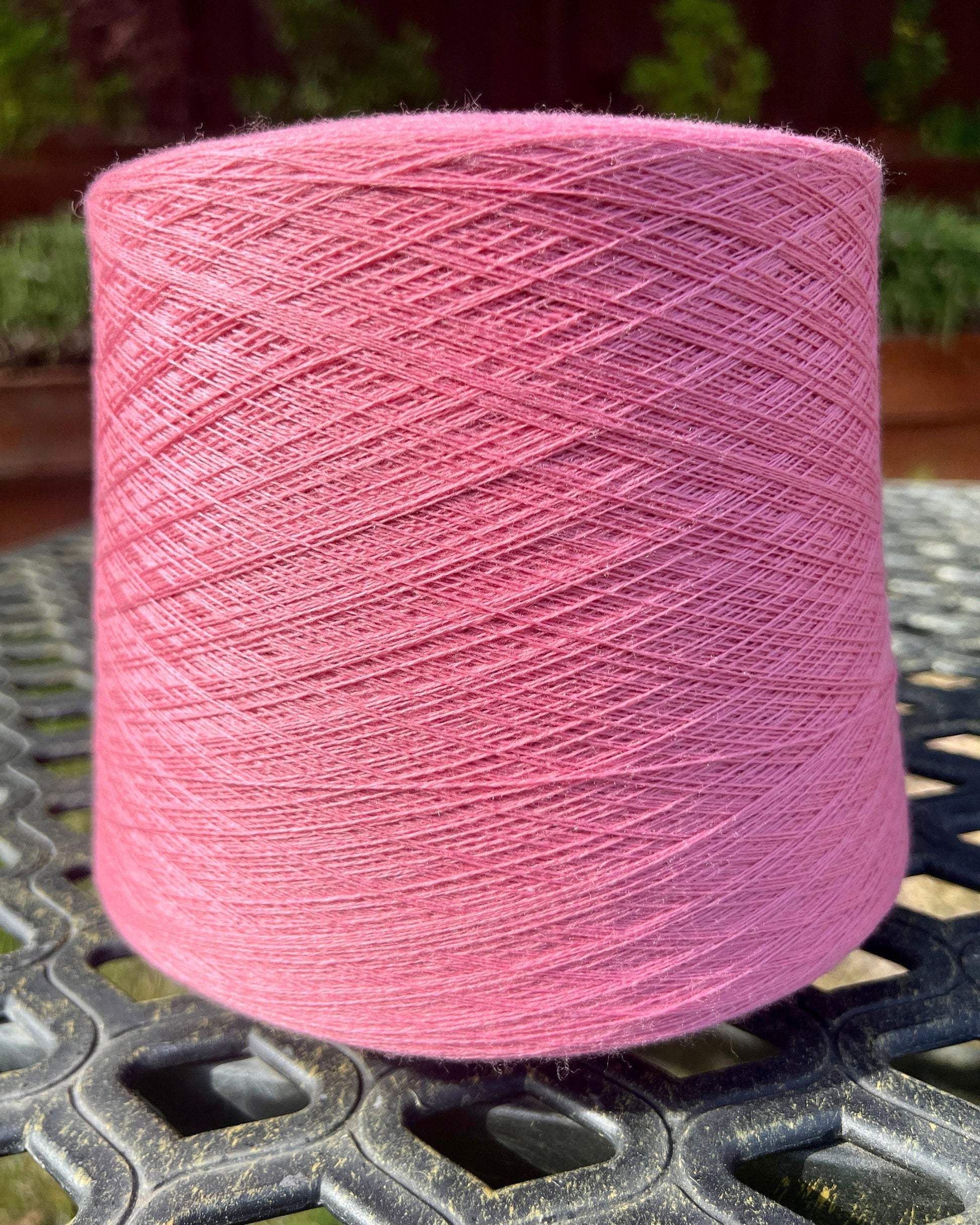 Pink spool of yarn on a metal surface with a blurred natural background