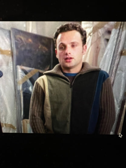 Man wearing a brown vest over a black jacket with a blue shirt underneath, standing in front of a store display.