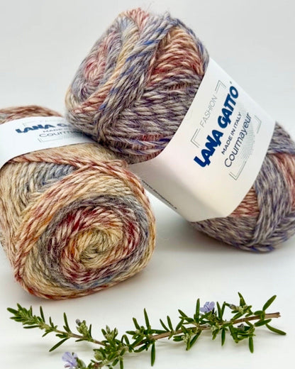 Two skeins of multicolored yarn with a label on a white background, accompanied by a sprig of rosemary.