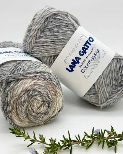 Two balls of gray yarn with a Lana Grossa label on a white background with a sprig of rosemary.