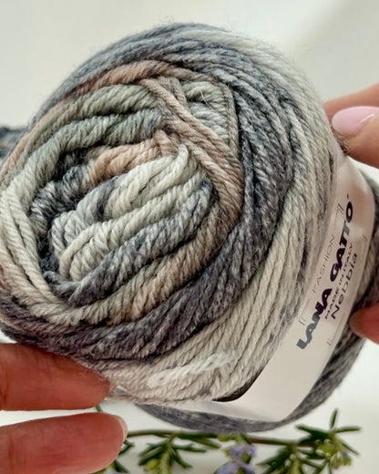 Ball of yarn with a brand label held by a hand against a light background
