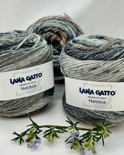 Three balls of Lana Gatto Nebbia yarn on a white background with a sprig of lavender.