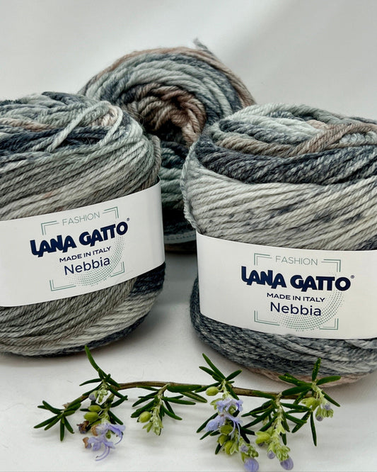 Three balls of Lana Gatto Nebbia yarn on a white background with a sprig of lavender.