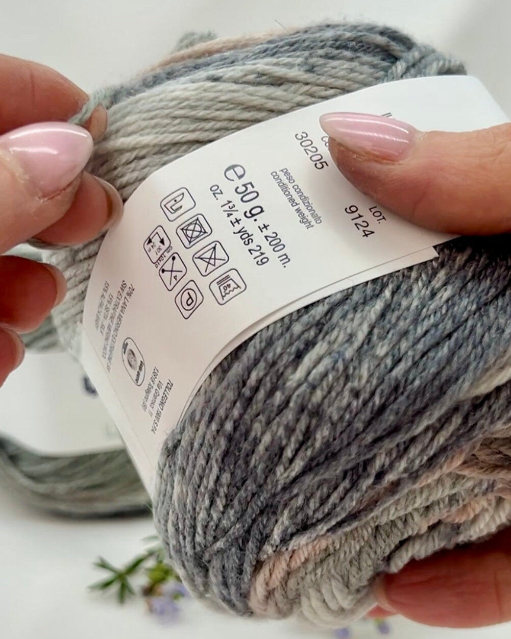 Ball of yarn with a label held by hands against a neutral background