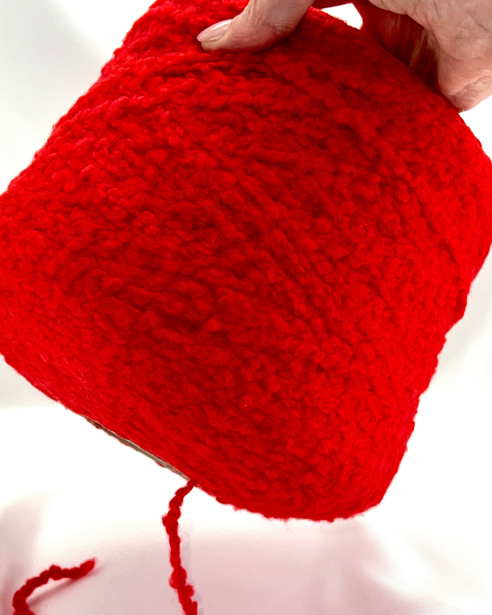Red knitted item held by a hand on a white background