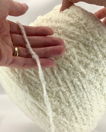 Close-up of hands holding a ball of white yarn with a plain background
