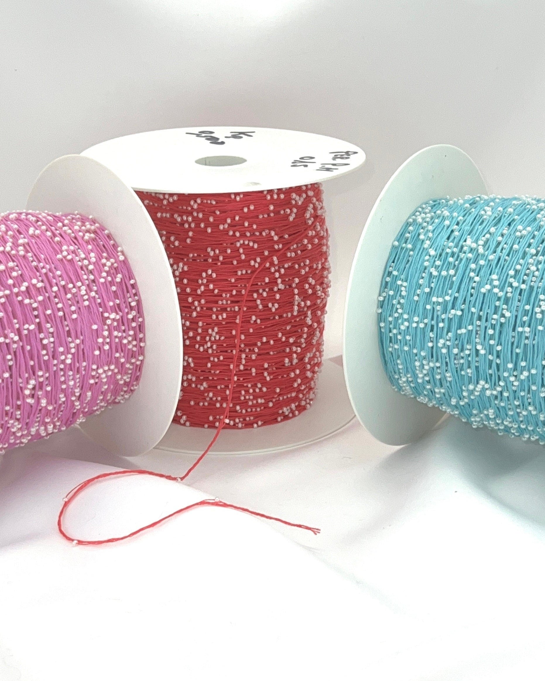 Three spools of thread in pink, red, and blue on a white background