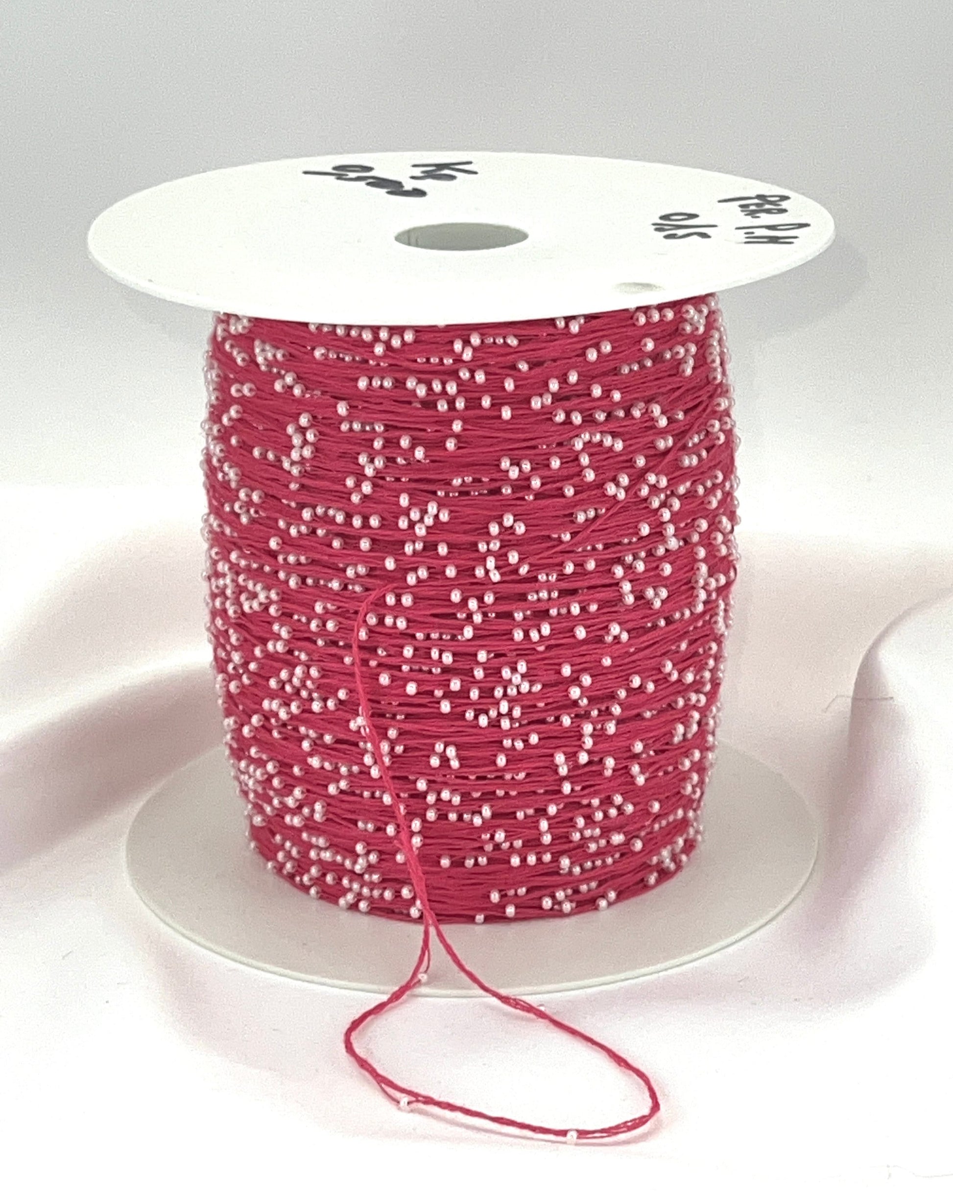 Spool of pink thread with white beads on a white background