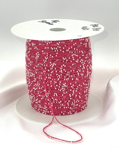Spool of pink thread with white beads on a white background