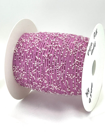 Spool of pink thread with white beads on a white background