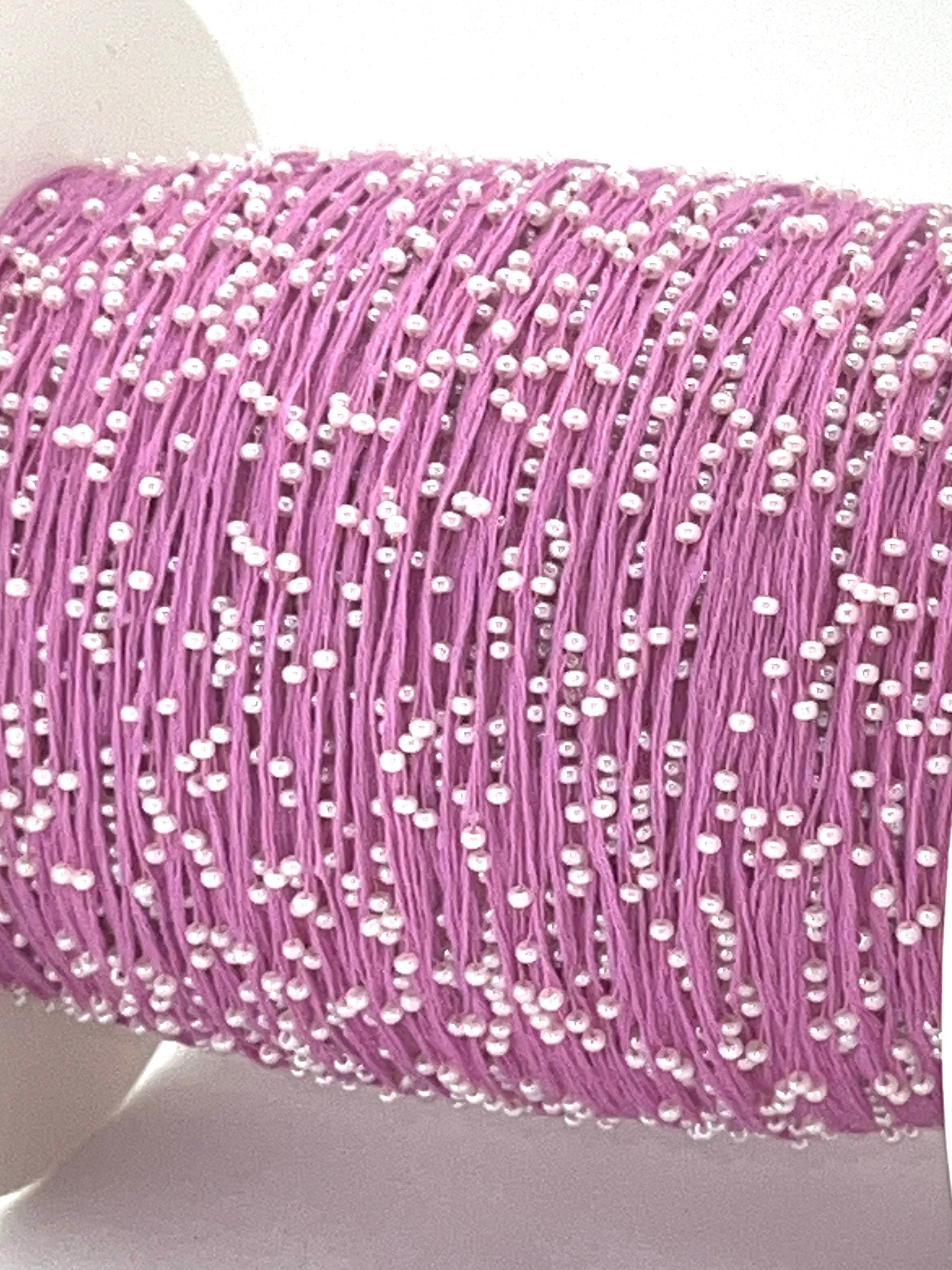 Spool of pink thread with white beads on a white background