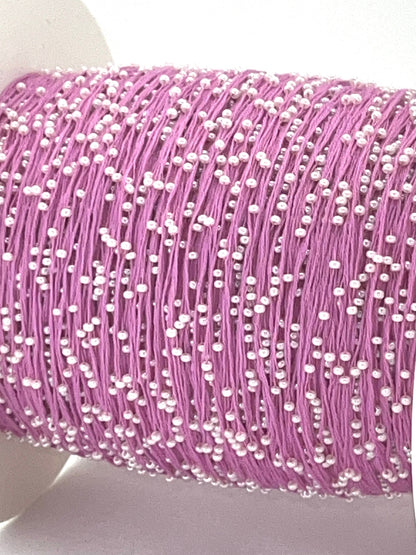 Spool of pink thread with white beads on a white background