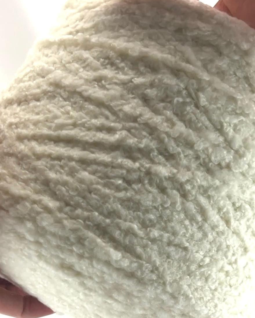 Close-up of a ball of white yarn held by hands against a white background