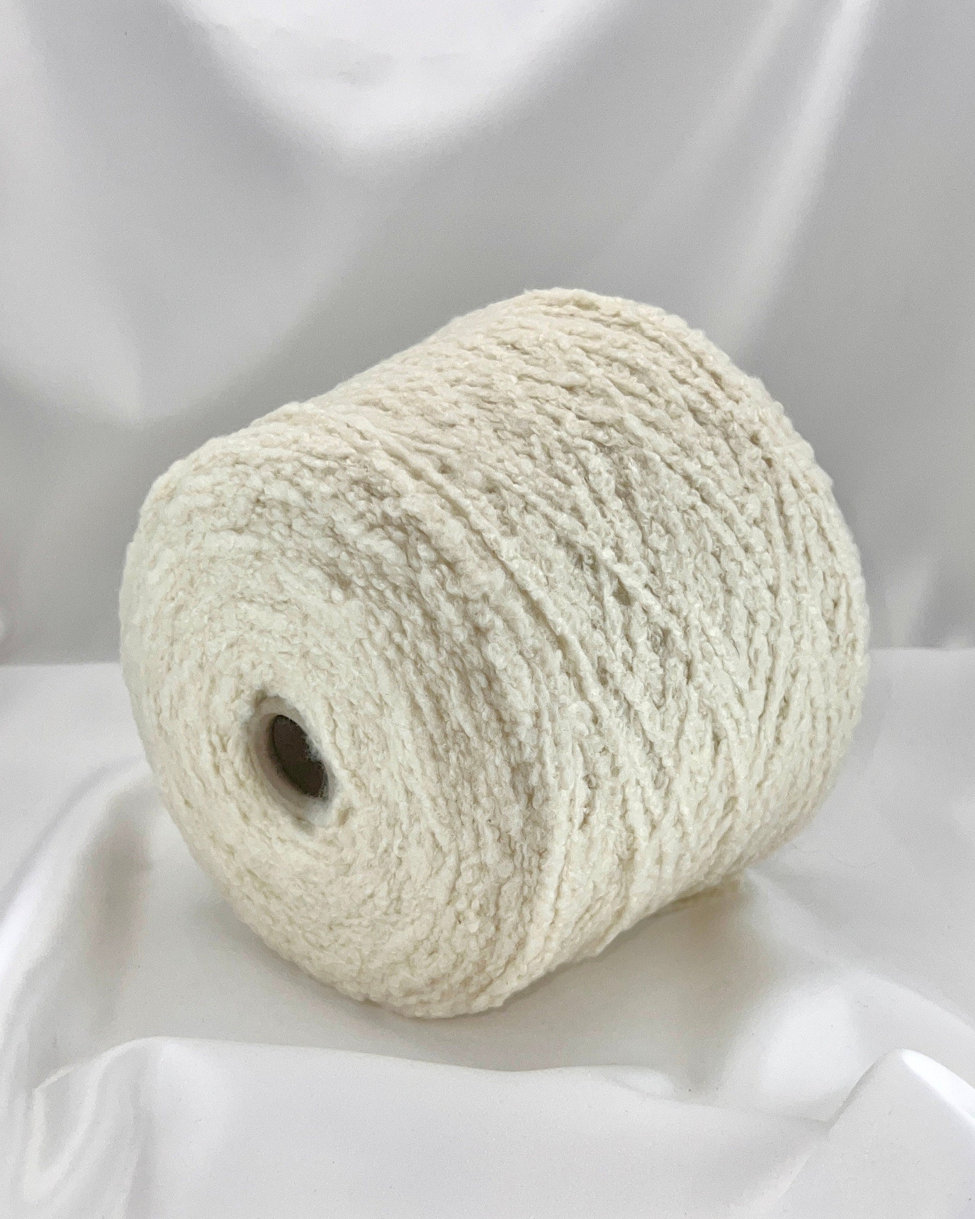 Roll of white yarn on a white fabric background