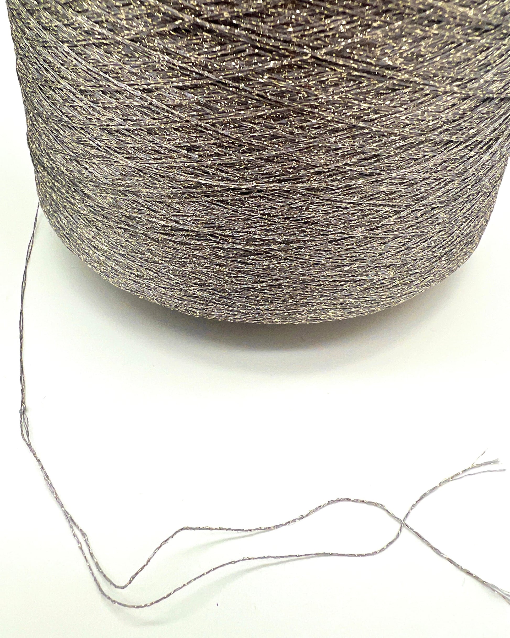 A professional cone of Kyototex MANNA-GROSSA metallic lamé yarn in Brushed Gold. The image shows the yarn's intense shimmer and fine texture, with detail shots of the fiber being held to demonstrate its lace-weight scale. Available at iDOKNiT.com.