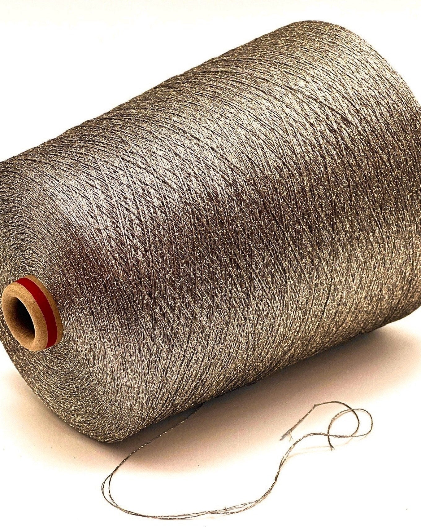 A professional cone of Kyototex MANNA-GROSSA metallic lamé yarn in Brushed Gold. The image shows the yarn's intense shimmer and fine texture, with detail shots of the fiber being held to demonstrate its lace-weight scale. Available at iDOKNiT.com.