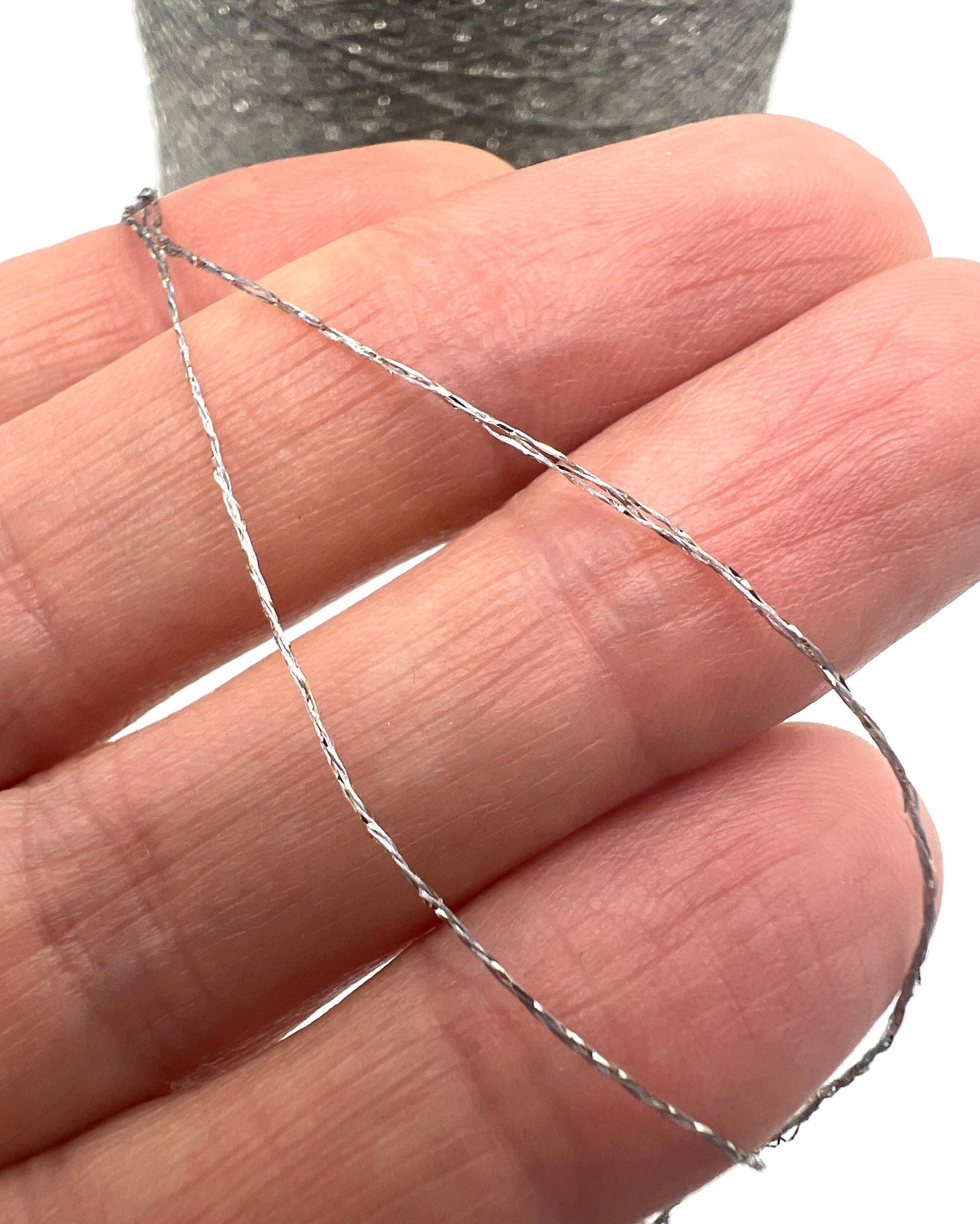 A professional cone of Kyototex MANNA-GROSSA metallic lamé yarn in Brushed Gold. The image shows the yarn's intense shimmer and fine texture, with detail shots of the fiber being held to demonstrate its lace-weight scale. Available at iDOKNiT.com.