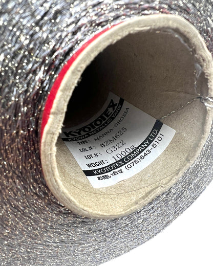 A professional cone of Kyototex MANNA-GROSSA metallic lamé yarn in Brushed Gold. The image shows the yarn's intense shimmer and fine texture, with detail shots of the fiber being held to demonstrate its lace-weight scale. Available at iDOKNiT.com.