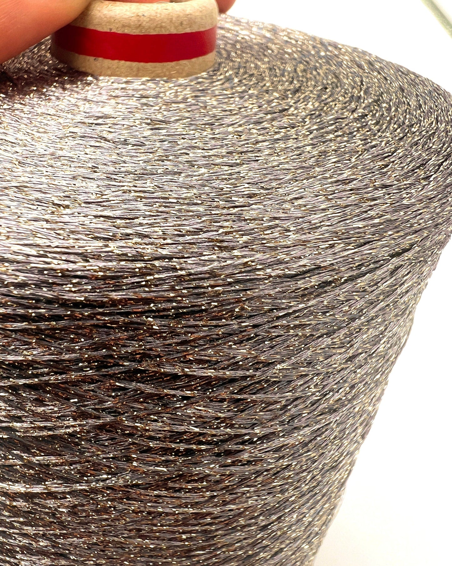 A professional cone of Kyototex MANNA-GROSSA metallic lamé yarn in Brushed Gold. The image shows the yarn's intense shimmer and fine texture, with detail shots of the fiber being held to demonstrate its lace-weight scale. Available at iDOKNiT.com.