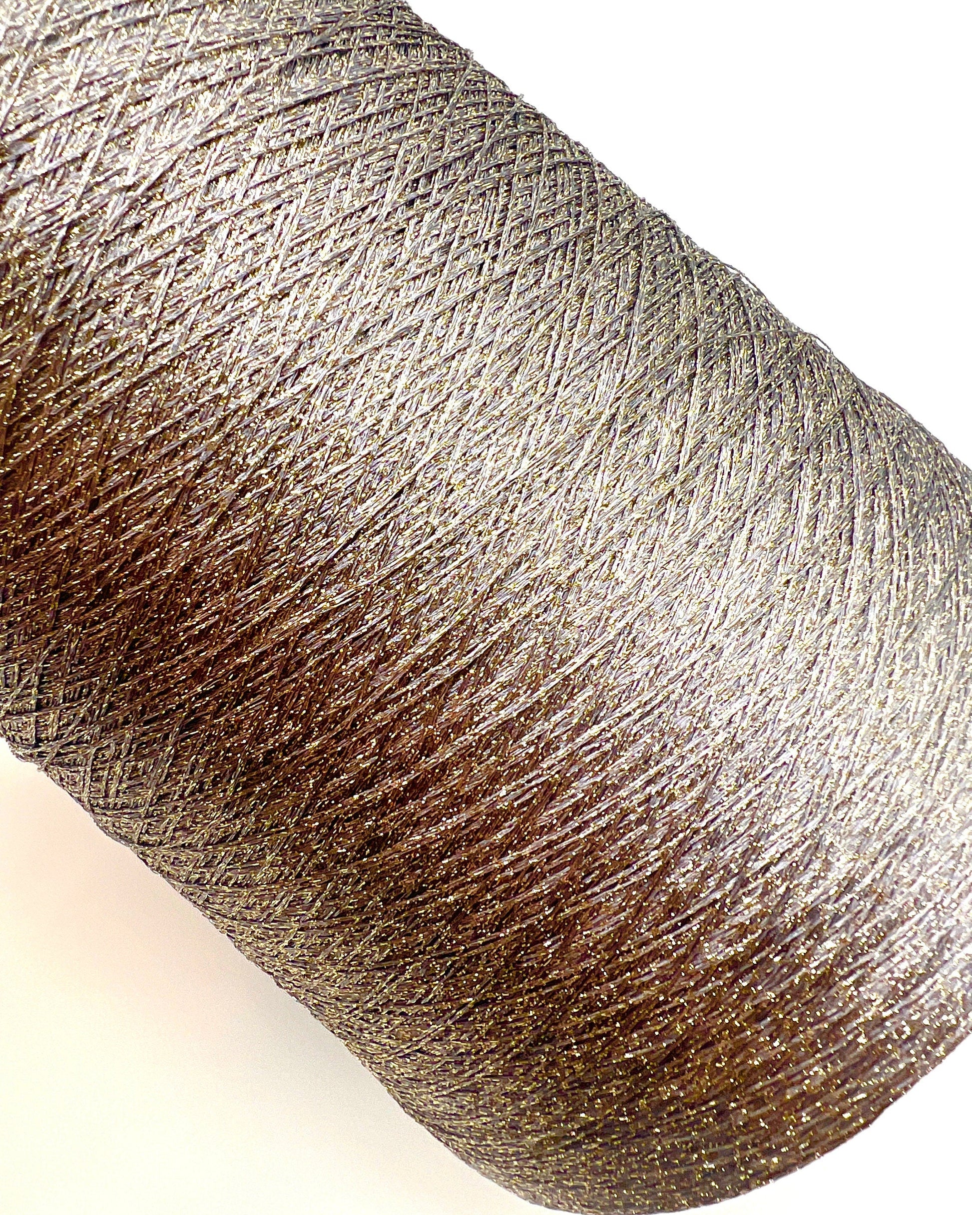 A professional cone of Kyototex MANNA-GROSSA metallic lamé yarn in Brushed Gold. The image shows the yarn's intense shimmer and fine texture, with detail shots of the fiber being held to demonstrate its lace-weight scale. Available at iDOKNiT.com.